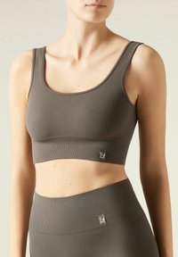 Brązowy prążkowany crop top wykonany z elastycznego materiału, z szerokimi ramiączkami i metką logo na dolnym brzegu. Gładka faktura z dopasowanym krojem.