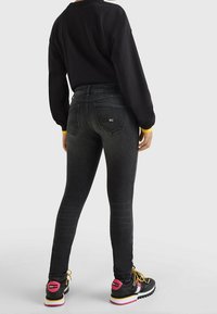Jeans skinny de cintura alta negros, mezcla de algodón, cinco bolsillos, costuras en contraste, combinados con zapatillas negras con acentos rosas y cordones amarillos.