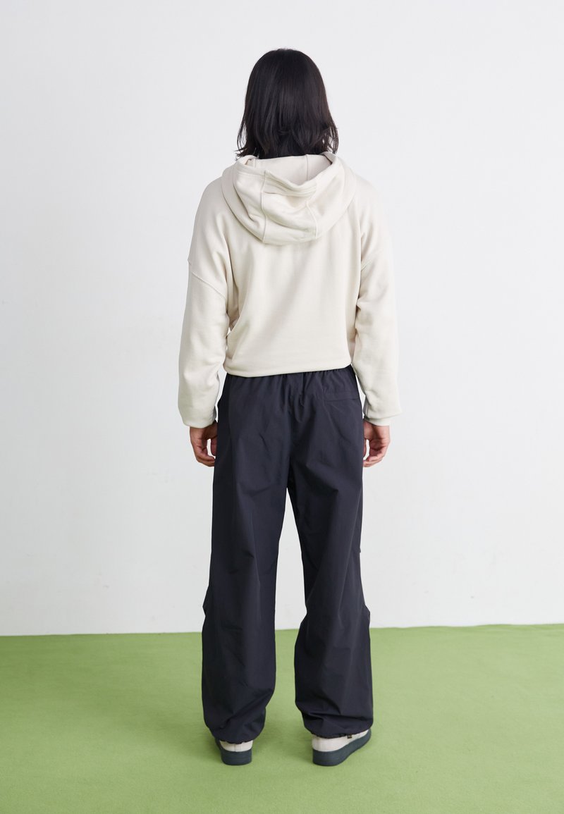 Hoodie beige clair avec un cordon de serrage à la capuche, associé à un pantalon noir ample. L'ensemble présente une coupe décontractée et une texture douce.