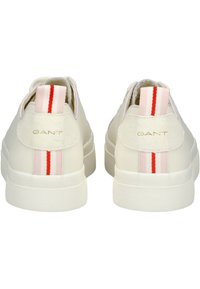 Sneaker bianche in pelle con suola in gomma testurizzata. Presentano dettagli in tessuto a strisce rosa e rosse sul tallone e un logo dorato "GANT".