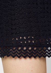 Tissu en dentelle noire crochetée avec un bord festonné sur une peau claire.