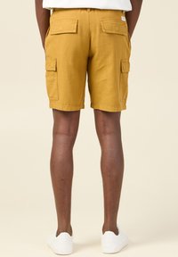 Pantalones cortos cargo de algodón en color mostaza, con dos bolsillos laterales, dos bolsillos traseros y un diseño de corte recto.