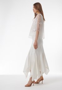 Blusa blanca de gasa con bordados florales, combinada con una falda blanca asimétrica y con capas. Calzado: sandalias transparentes con tacón.