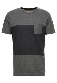 Camiseta corta de manga gris con un diseño de bloques de color que incluye secciones en gris oscuro y gris claro, y un pequeño bolsillo en el pecho. Material suave de mezcla de algodón.
