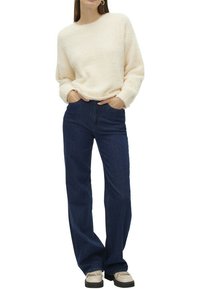 Pull en texture crème avec un col rond, associé à un jean flare en denim bleu foncé taille haute et des chaussures de couleur claire.