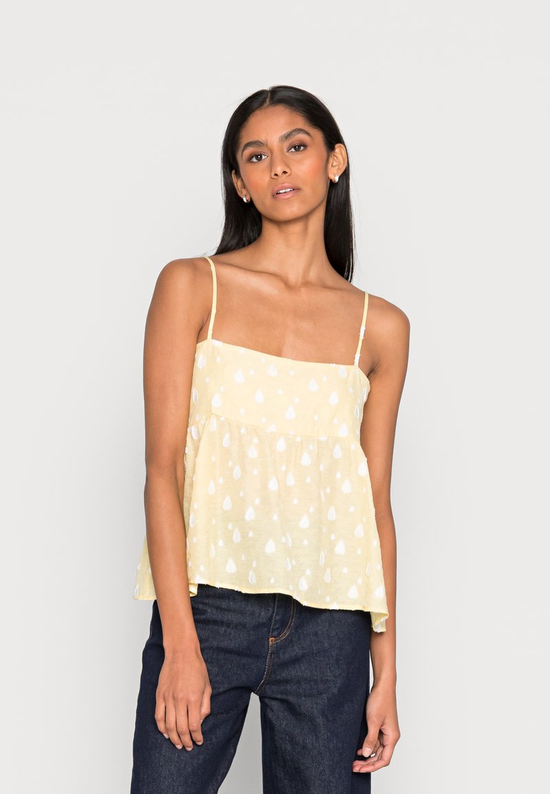 Top amarelo sem mangas com decote quadrado, apresentando um tecido texturizado e padrões em forma de gota brancos por toda a peça. Caimento solto com um design em camadas.