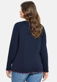 Námořnický top s dlouhým rukávem a zakřiveným lemem, s růžovým volánkem na dolním okraji. Vyroben z měkkého materiálu, vhodný pro volný čas.