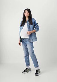 Chaqueta de mezclilla azul clara sobre una blusa blanca, combinada con jeans azul claro y zapatillas deportivas negras con detalles verdes. Diseño simple, corte relajado.