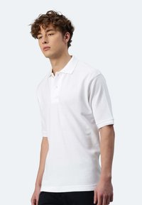 Polo shirt bianco a maniche corte, con colletto classico e una patta di chiusura con tre bottoni. Realizzato in tessuto di cotone testurizzato.