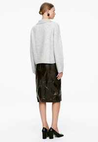 Grauer, übergroßer Strickpullover mit weitem Kragen, kombiniert mit einem glänzenden, schwarzen Bleistiftrock mit einem Schlitz hinten und schwarzen, hochhackigen Schuhen.