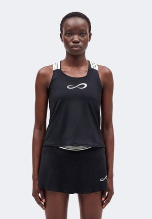 Femme portant un haut sans manches noir avec des rayures blanches aux épaules et une jupe noire avec un petit logo blanc sur le côté gauche.