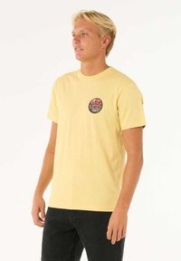 Geel katoenen t-shirt met een ronde grafische logo op de borst. De pasvorm is relaxte met korte mouwen en een ronde halslijn.