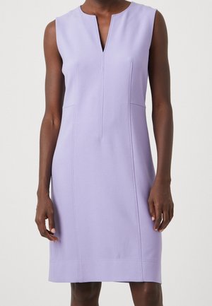 Robe lavande sans manches, longueur au genou, avec encolure en V à l'avant et coutures verticales visibles portée par une personne debout.