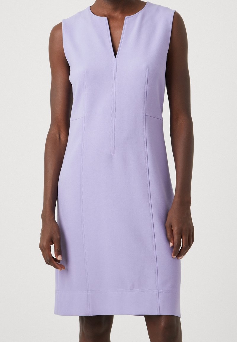 Robe lavande sans manches, longueur au genou, avec encolure en V à l'avant et coutures verticales visibles portée par une personne debout.