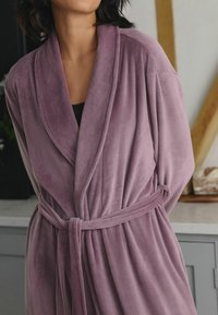 Lilla korduroystickade hommikumantlid laienevate krae ja nöörvööga, millel on vertikaalne ribakonstruktsioon ja lõdva istuvusega.