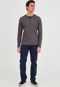 Grå langermet skjorte med en kontrasterende mørk halslinning, kombinert med marineblå bukser og svarte sneakers. Enkel design, uformell passform.