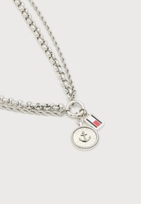 Διπλό ασημένιο κολιέ αλυσίδας με στρογγυλό φυλαχτό άγκυρας και ορθογώνιο φυλαχτό με κόκκινη, λευκή και μπλε σημαία σε λευκό φόντο.