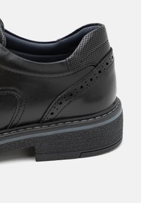 Chaussure en cuir noir avec un talon texturé, des accents perforés et une semelle épaisse et texturée. Comprend une bande contrastante gris clair.