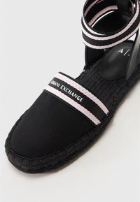 Sandale espadrile negre, cu un superior din pânză, talpă din jute împletit și curele elastice cu accente roz și alb. Marca este "Armani Exchange."