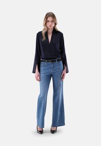 Blusa di raso blu navy con scollatura a V profonda e maniche a campana, abbinata a jeans a gamba larga blu chiaro e scarpe con tacco nere. Cintura nera inclusa.