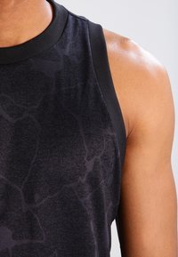 Svart ärmlös träningströja i atletisk stil med en texturerad design, med en slät halsringning och kontrasterande svart kant längs axlarna.