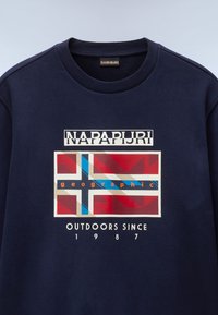 Sudadera azul marino con un estampado gráfico de una bandera en colores rojo, azul y beige, con el logo "NAPAPIJRI" y el texto "OUTDOORS SINCE 1987".