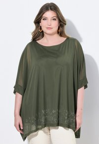 Top verde oliva, dal taglio morbido e con maniche corte, in tessuto soffice e con un design floreale ricamato all'orlo. Abbinato a pantaloni chiari.