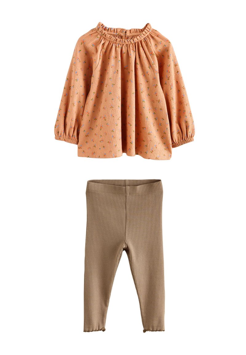 Blouse orange à motif floral avec encolure froncée et manches longues, associée à des leggings côtelés beiges. Les deux sont en coton à texture douce.