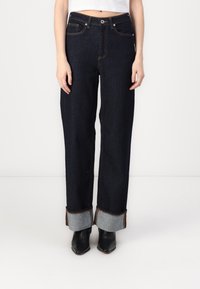 Jeans de tiro alto azul oscuro con un ajuste holgado, que presentan puños enrollados en un tono más claro de denim y costuras en contraste a lo largo de las costuras.