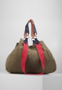 Olive green bag with red fabric straps and navy leather accents. Rounded shape, silver hardware rings. Soft texture throughout.