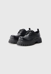 Scarpe di pelle nera con punta arrotondata, suola spessa e strutturata, e design con lacci. Presentano una linguetta sul tallone e occhielli metallici per i lacci.