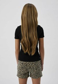 Svart kortärmad skjorta i kombination med beige leopardmönstrade shorts. Långt, rakt brunt hår som faller ner längs ryggen. Enkel design.