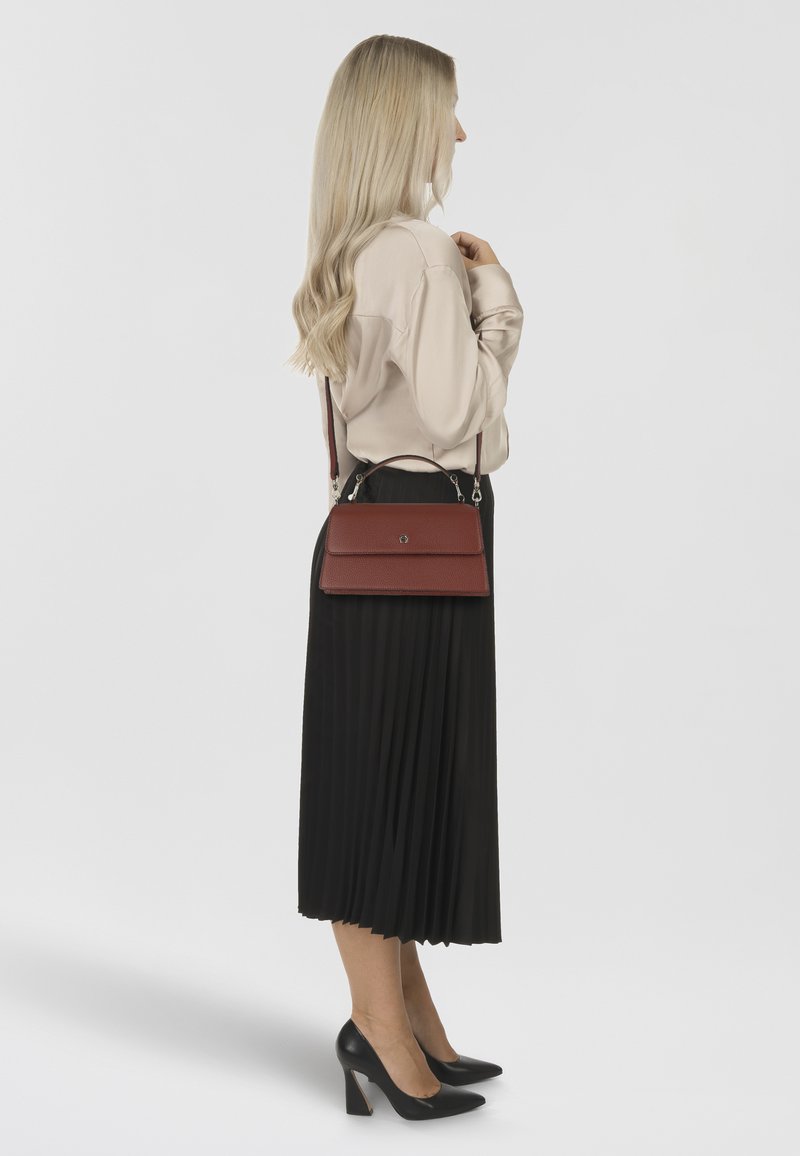 Rode leren handtas met een vlak voorflapje, verstelbare riem en zilveren beslag. Gecombineerd met een crèmekleurige blouse en een zwarte geplooide rok.