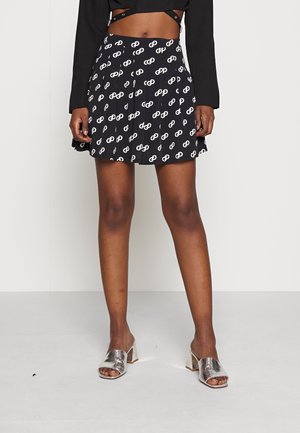 Czarna plisowana spódnica z białym wzorem okrągłych motywów. Połączona z błyszczącymi, srebrnymi mulesami na klockowym obcasie, prezentując nowoczesny wygląd.