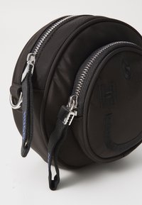Borsa rotonda in tessuto nero con doppie cerniere argentate, lettere ricamate e dettagli testurizzati; presenta cinturini a contrasto per una facile maneggevolezza.