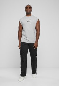 Grå utenermet t-skjorte med logo, sammen med svarte cargobukser. Outfiten kompletteres av hvite joggesko med minimale detaljer.