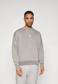 Γκρι φούτερ με στρογγυλή λαιμόκοψη, ελαστικά μανσέτες και τελείωμα. Διαθέτει μικρό λογότυπο στο στήθος. Φοριέται με ανοιχτό γκρι παντελόνι φόρμας.