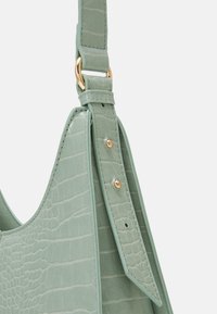 Borsa a mano in pelle verde embossata con coccodrillo, dotata di una chiusura in metallo dorato, cintura regolabile con rivetti e una texture liscia.