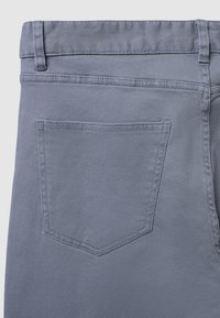 Graue Denim-Hose mit einer Gesäßtasche mit spitzem oberen Ende und subtilen Steppdetails. Der Stoff hat eine glatte, strukturierte Oberfläche.