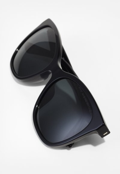 Black oversized sunglasses with dark lenses. Smooth plastic frame, angular design, and subtle metallic accents at the temples.