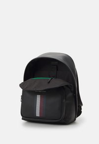 Zaino nero realizzato in materiale sintetico liscio. Presenta una tasca frontale con zip e un design multistrisce, con una zip di accento verde.