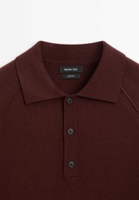 Bordeaux wollen polo shirt met een klassieke kraag, voorzien van drie zwarte knopen en een zachte, gestructureerde brei-stof. Merkenlabel op de kraag.