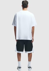 Tricou alb cu mânecă scurtă și pantaloni scurți sport negri cu accente albe. Țesătura pare ușoară; croiala este lejeră. Șosete albe și pantofi completează ținuta.