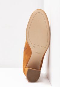 Chaussure pour femme en suède marron vue de la semelle, avec un talon carré bas et une marque de taille 4½, placée sur fond blanc.