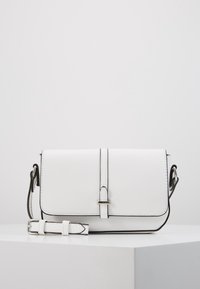 Vit läder crossbody-väska med klaffstängning, kontrasterande svart sömnad, justerbar rem och metalliska detaljer.