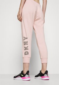 Rosa sweatshirtbyxor med manchetter har DKNY-märke i svart på sidan. Bärs med svarta och rosa träningsskor, vilket visar en avslappnad stil.