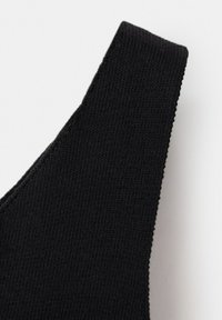 Gros plan sur un tissu noir tricoté avec une large sangle, montrant une texture détaillée et des coutures sur un fond uni.