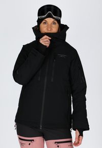 Black snow jacket with multiple zippered pockets, high collar, adjustable cuffs, and ventilation zips, paired with pink ski pants.