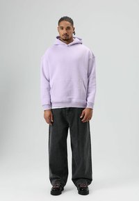 Lichtpaarse oversized hoodie met een voorzak, geribbelde manchetten en zoom, gecombineerd met baggy donkergrijze jeans en zwarte chunky schoenen.