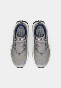 Grijze sportschoenen met een bovenkant van geribbelde mesh en paarse accenten. Voorzien van veters, een gevoerde tong en een witte zool met subtiele merkdetails.